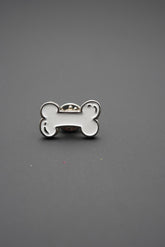 Pin metálico personalizado en forma de hueso blanco sobre fondo gris
