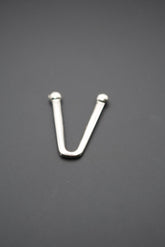 Gancho metálico en forma de V con extremos redondeados sobre fondo gris