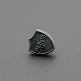 Botón de golpe en forma de escudo con grabado 'Signos' sobre fondo gris