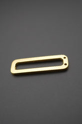 Etiqueta metálica rectangular dorada con textura diagonal, vista sobre fondo gris