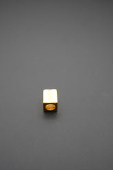 Cuenta metálica dorada de forma cuadrada con letra A grabada vista superior