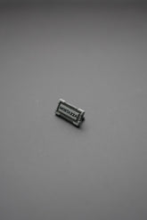 Etiqueta metálica rectangular con texto 'MOSTAZZA' en relieve sobre fondo gris