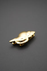 Pin metálico dorado en forma de concha marina sobre fondo gris oscuro vista lateral