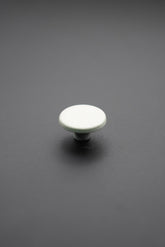 Botón metálico blanco redondo visto desde arriba sobre fondo gris oscuro