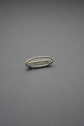 Remache ovalado metálico con la marca Leandrus sobre fondo gris