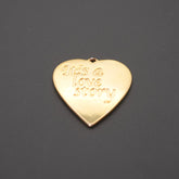 Colgante dorado en forma de corazón con grabado 'It's a love story' sobre fondo gris