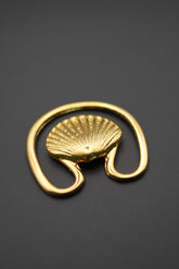 Gancho decorativo dorado con forma de concha sobre fondo negro, vista frontal
