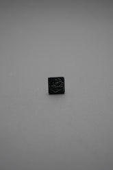 Botón de golpe negro cuadrado con diseño grabado en relieve visto de frente