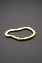 Pulsera dorada con forma orgánica y superficie pulida vista lateral