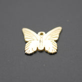 Dije metálico dorado con forma de mariposa visto desde arriba sobre fondo gris