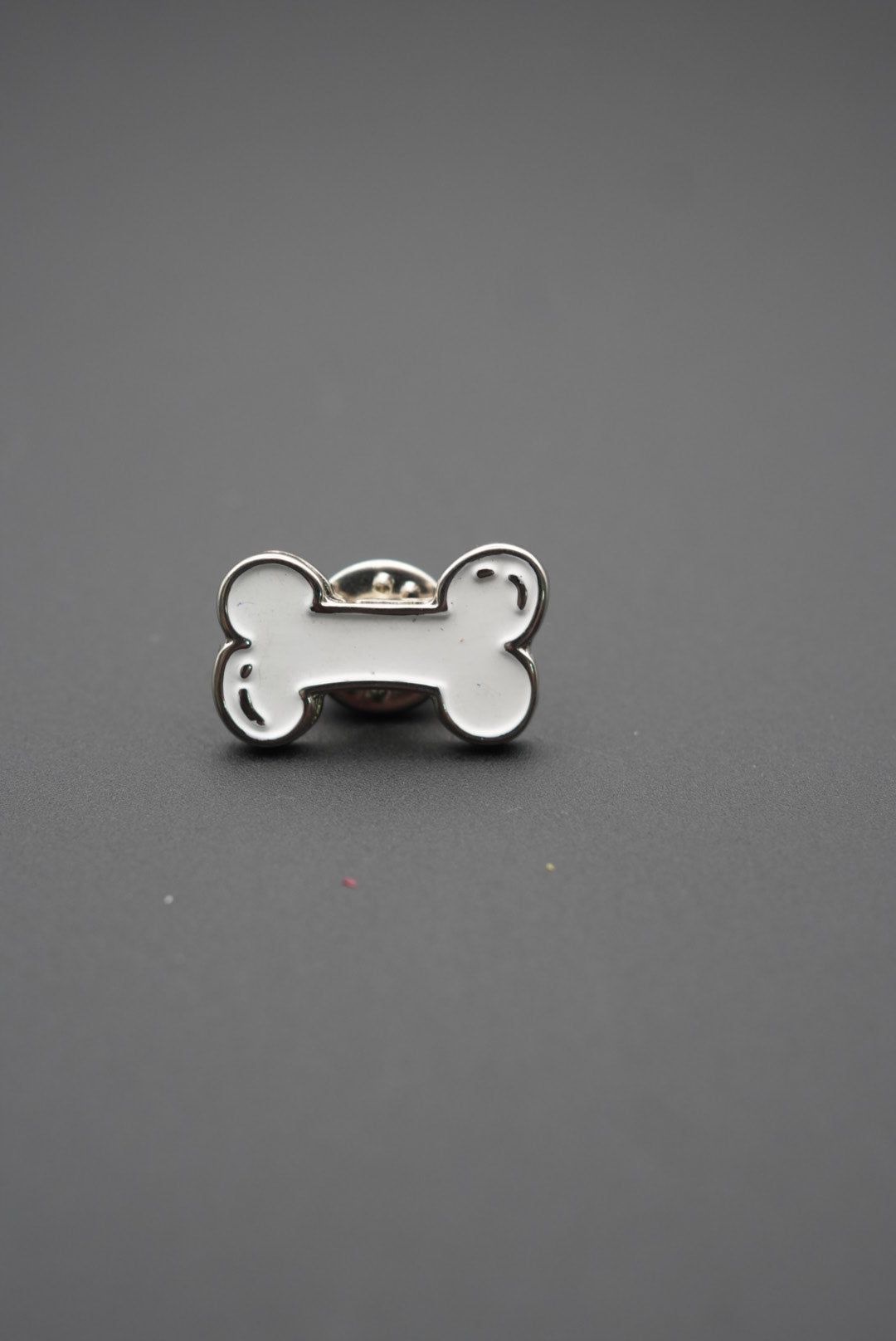 Pin metálico personalizado en forma de hueso blanco sobre fondo gris
