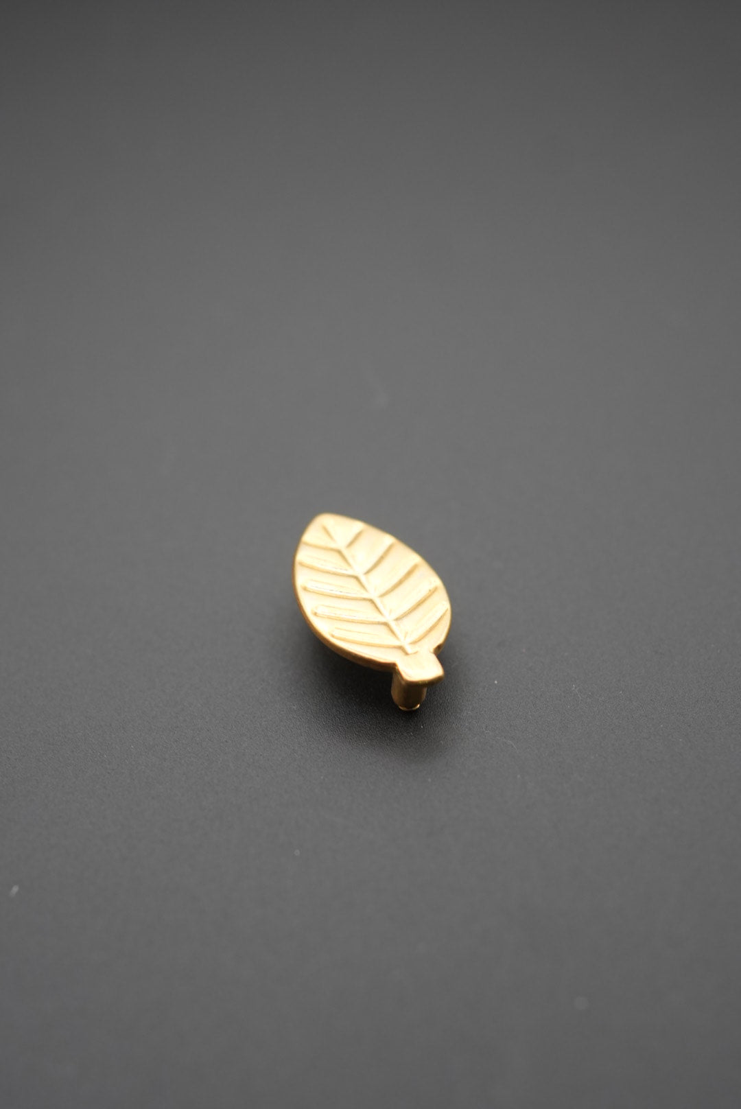 Tirador metálico dorado en forma de hoja sobre fondo gris