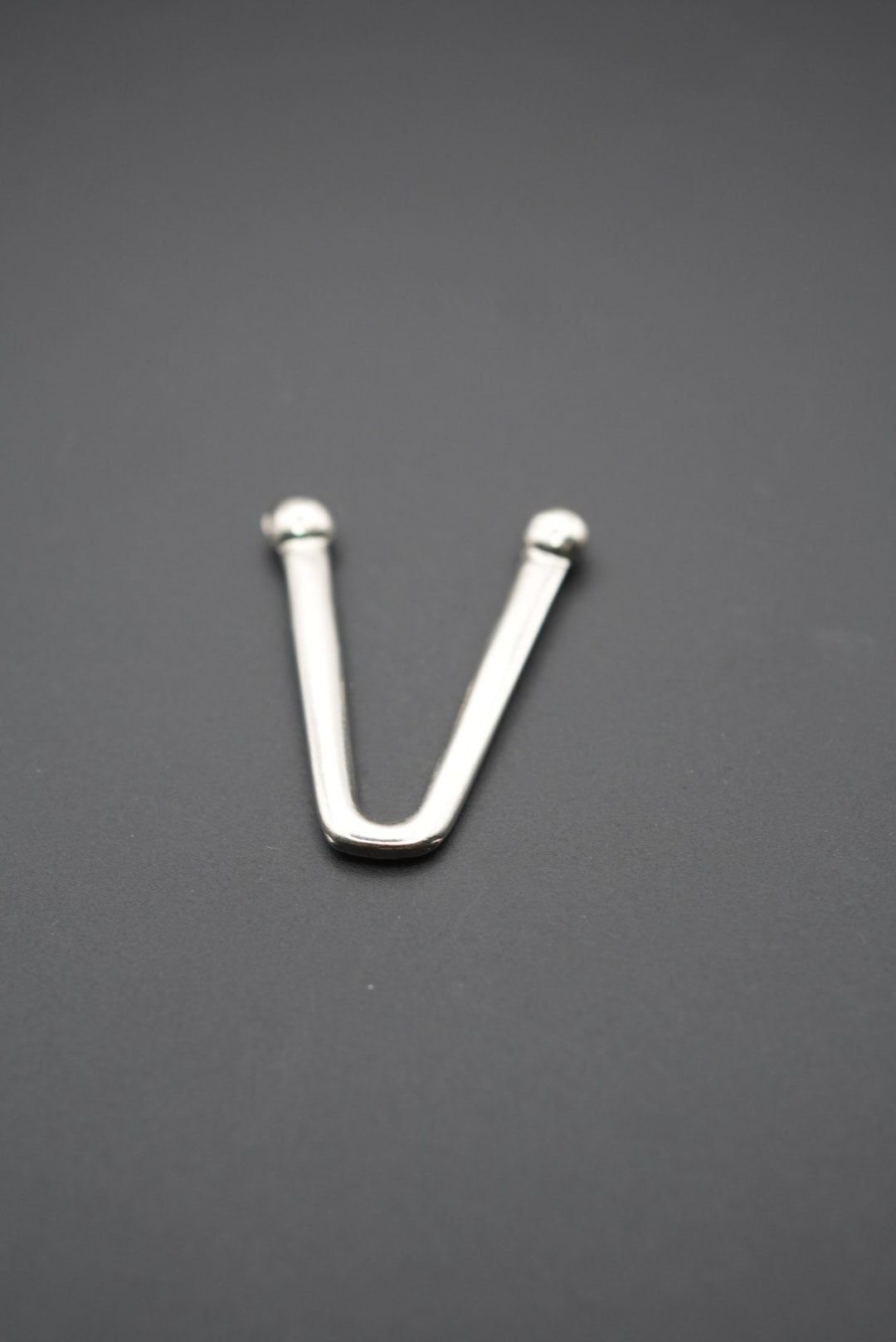 Gancho metálico en forma de V con extremos redondeados sobre fondo gris