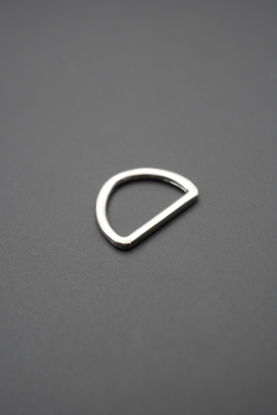 Arco metálico tipo D color plateado con acabado brillante sobre fondo gris