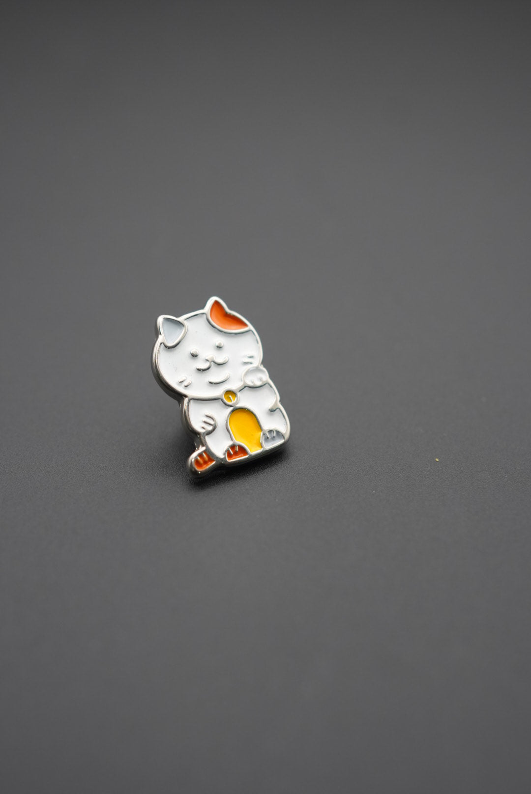 Pin personalizado con diseño de gato Maneki-neko en colores blanco, naranja y amarillo sobre fondo gris