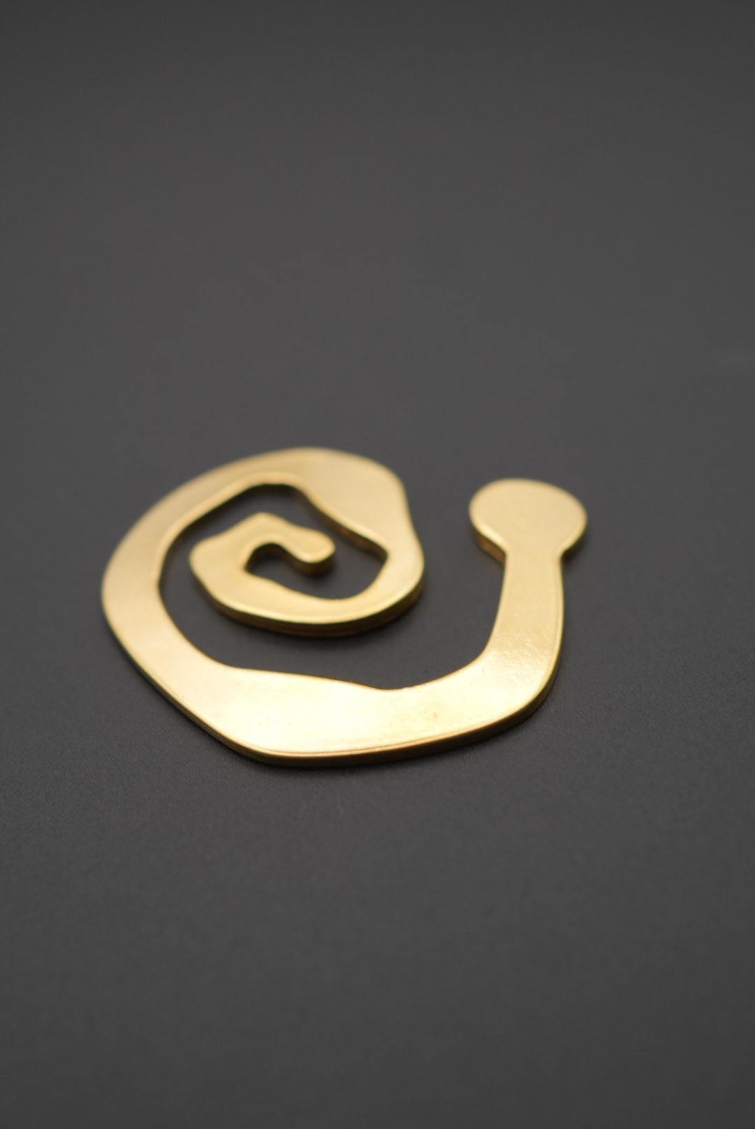 Broche dorado en forma de espiral sobre fondo gris oscuro, vista frontal