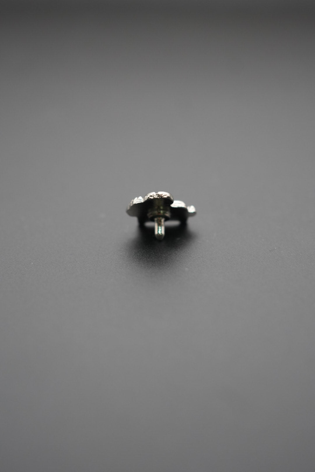 Pin metálico vista frontal sobre fondo gris