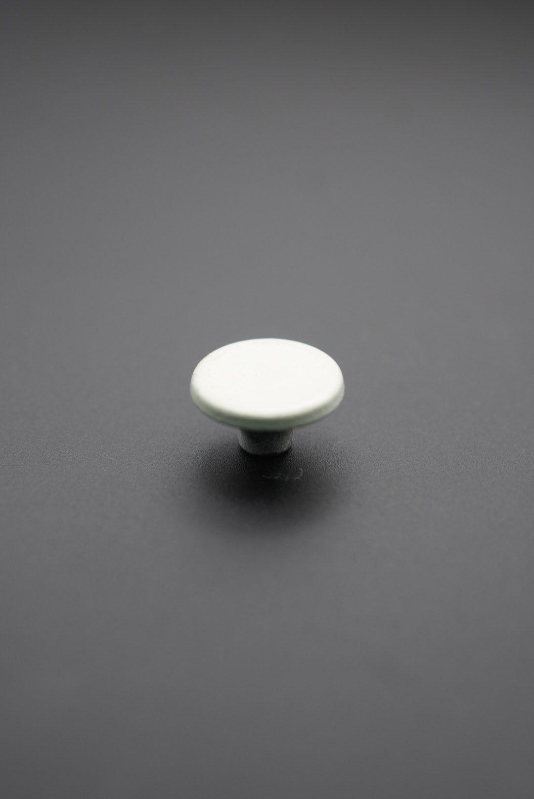 Botón metálico blanco redondo visto desde arriba sobre fondo gris oscuro