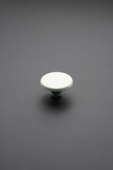 Botón metálico blanco redondo visto desde arriba sobre fondo gris oscuro