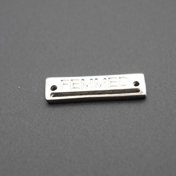 Placa metálica rectangular con grabado FEMMED sobre fondo gris