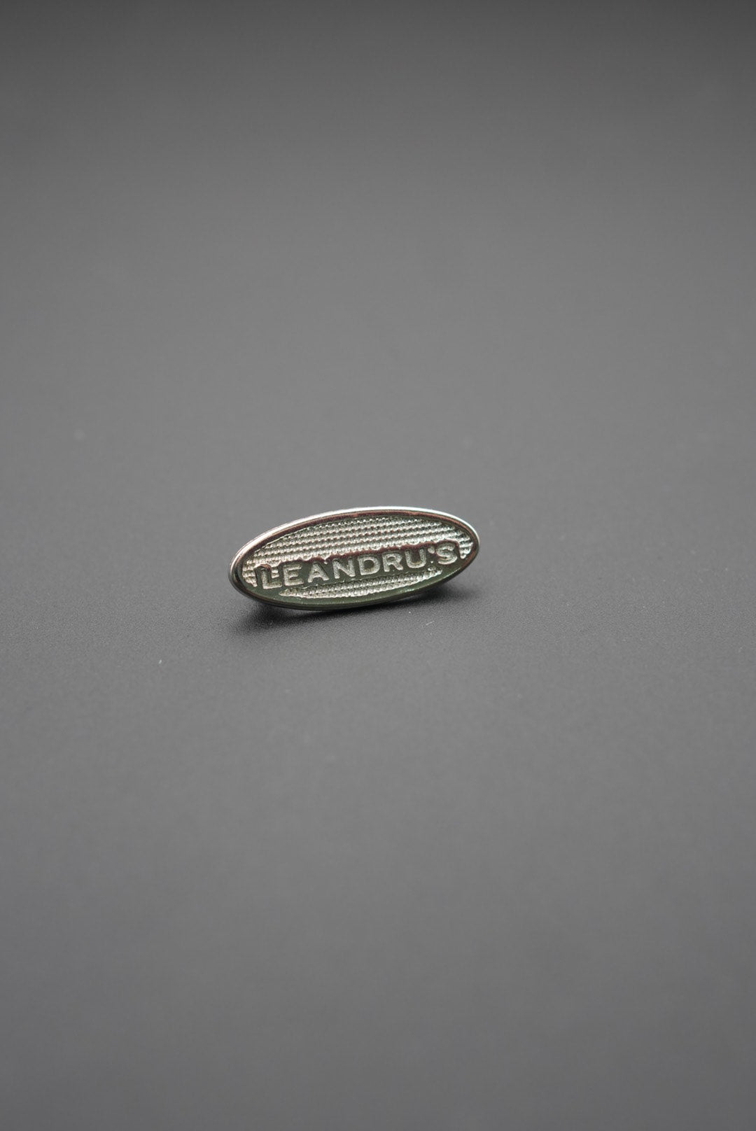Remache ovalado metálico con la marca Leandrus sobre fondo gris