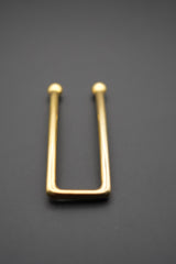 Pasador metálico dorado visto de frente sobre fondo gris