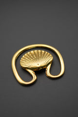 Gancho decorativo dorado con forma de concha sobre fondo negro, vista frontal