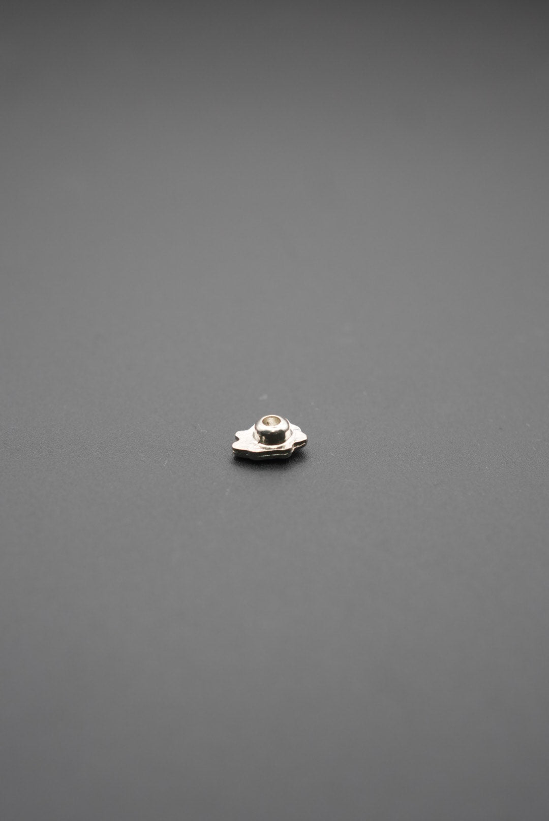 Pasador de metal pequeño con diseño floral en acabado plata sobre fondo gris