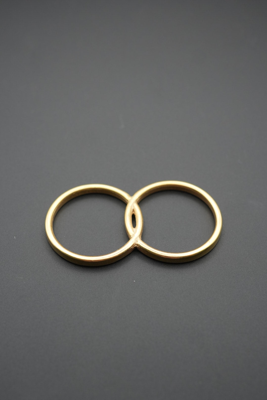 Anillo doble de latón pulido con acabado dorado sobre fondo gris oscuro
