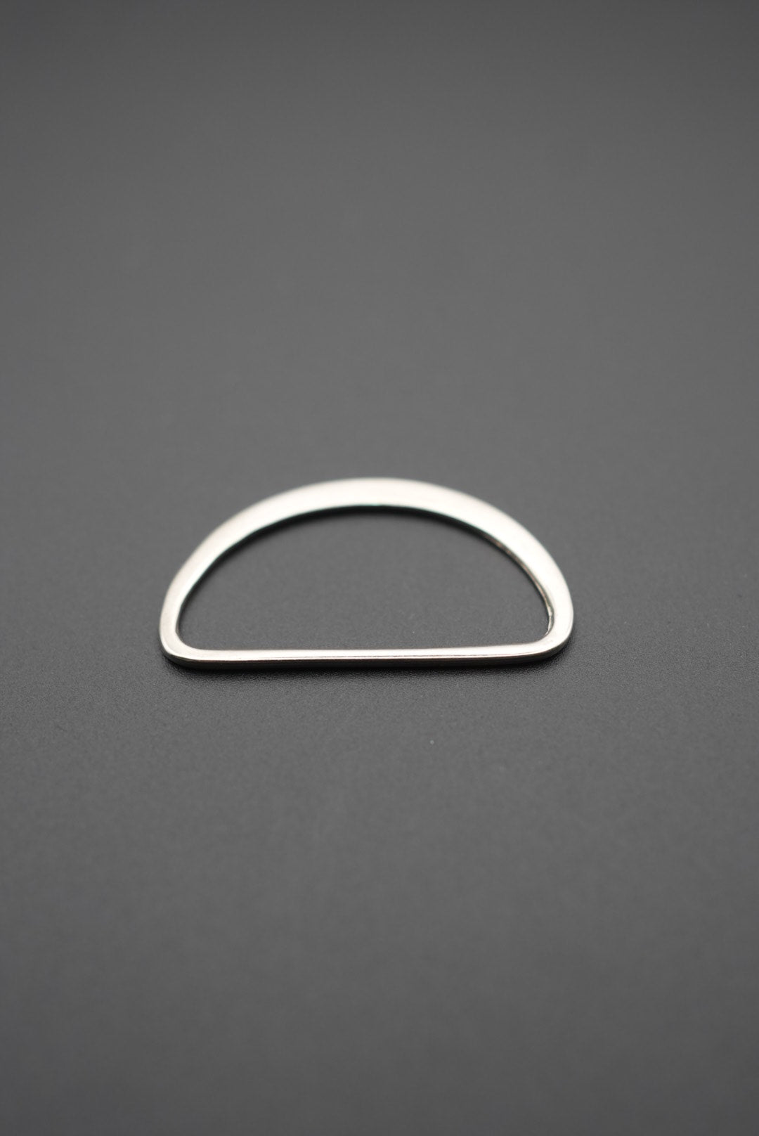 Argolla D plana metálica con acabado pulido vista frontal sobre fondo gris