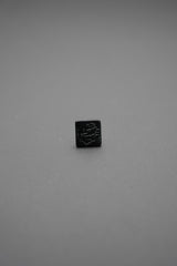 Botón de golpe negro cuadrado con diseño grabado en relieve visto de frente