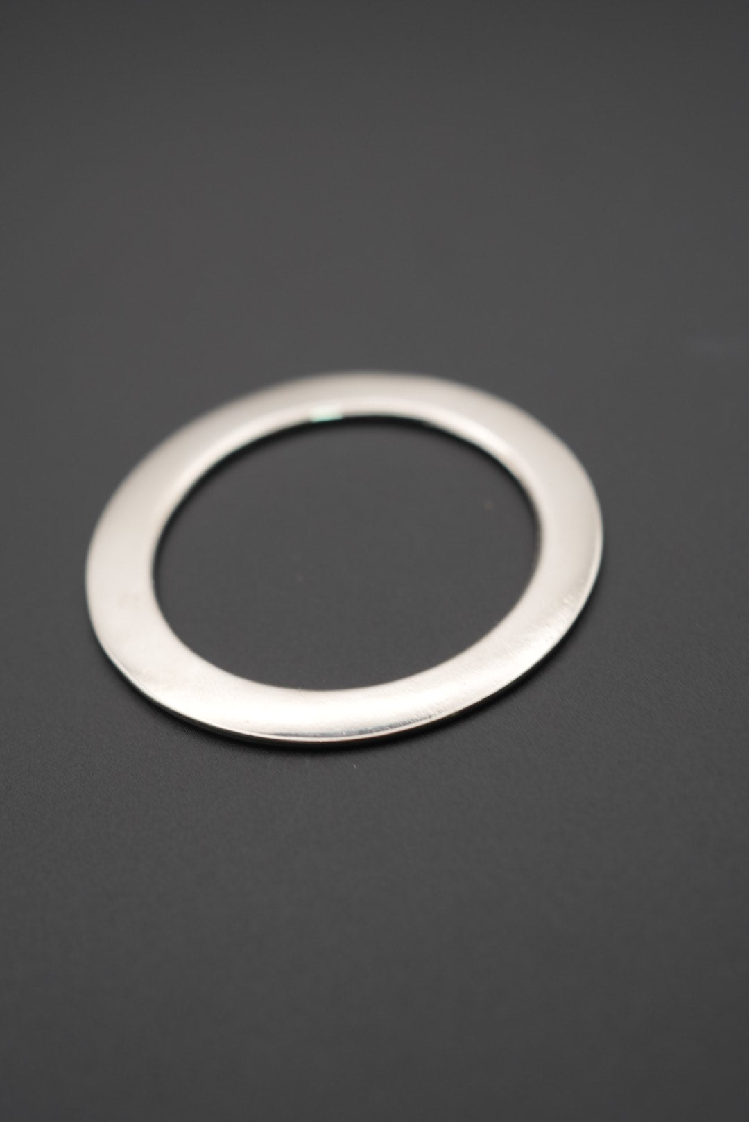 Arandela metálica circular con acabado pulido sobre fondo gris oscuro