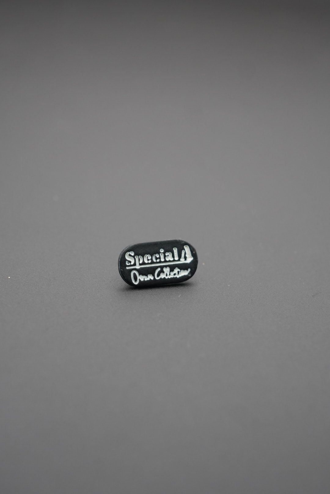 Remache ovalado negro con inscripción blanca special own collection sobre fondo gris
