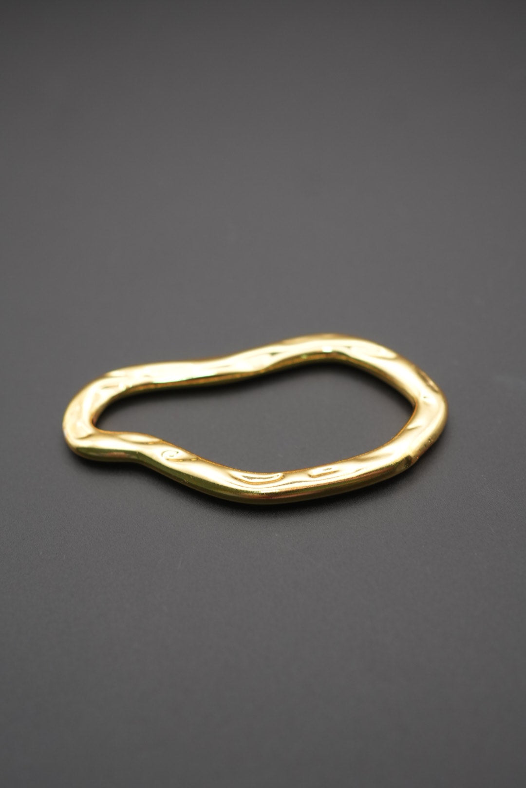Pulsera dorada con forma orgánica y superficie pulida vista lateral