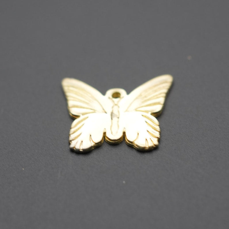Dije metálico dorado con forma de mariposa visto desde arriba sobre fondo gris