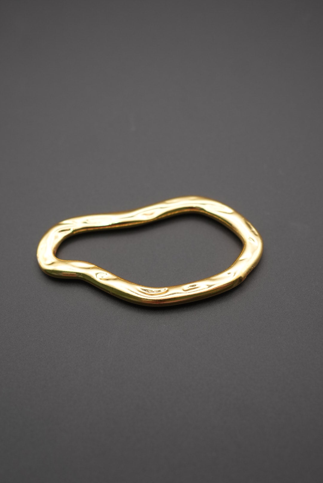 Pulsera de metal dorado con diseño irregular sobre fondo gris oscuro