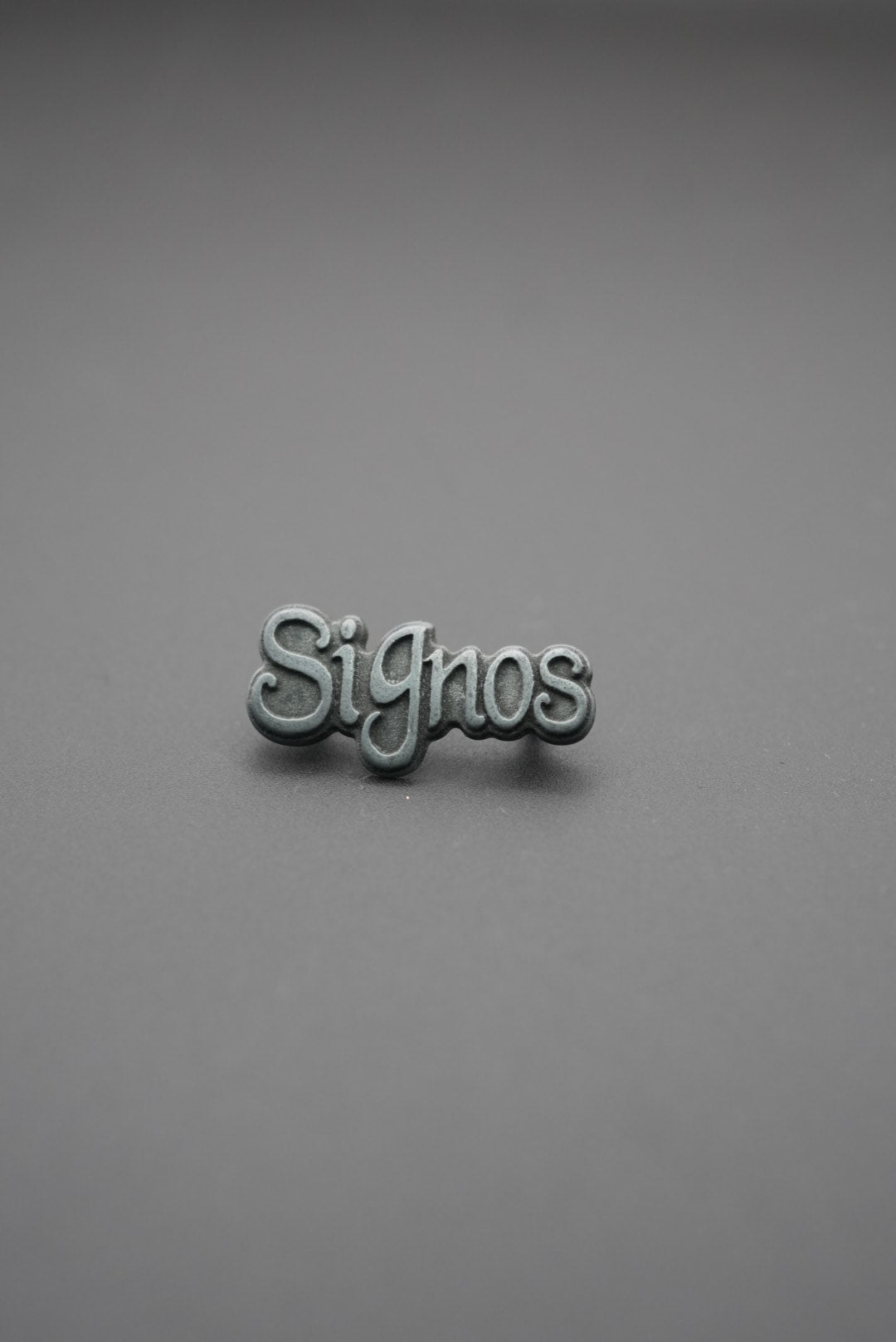 Remache con texto 'Signos' acabado envejecido sobre fondo gris
