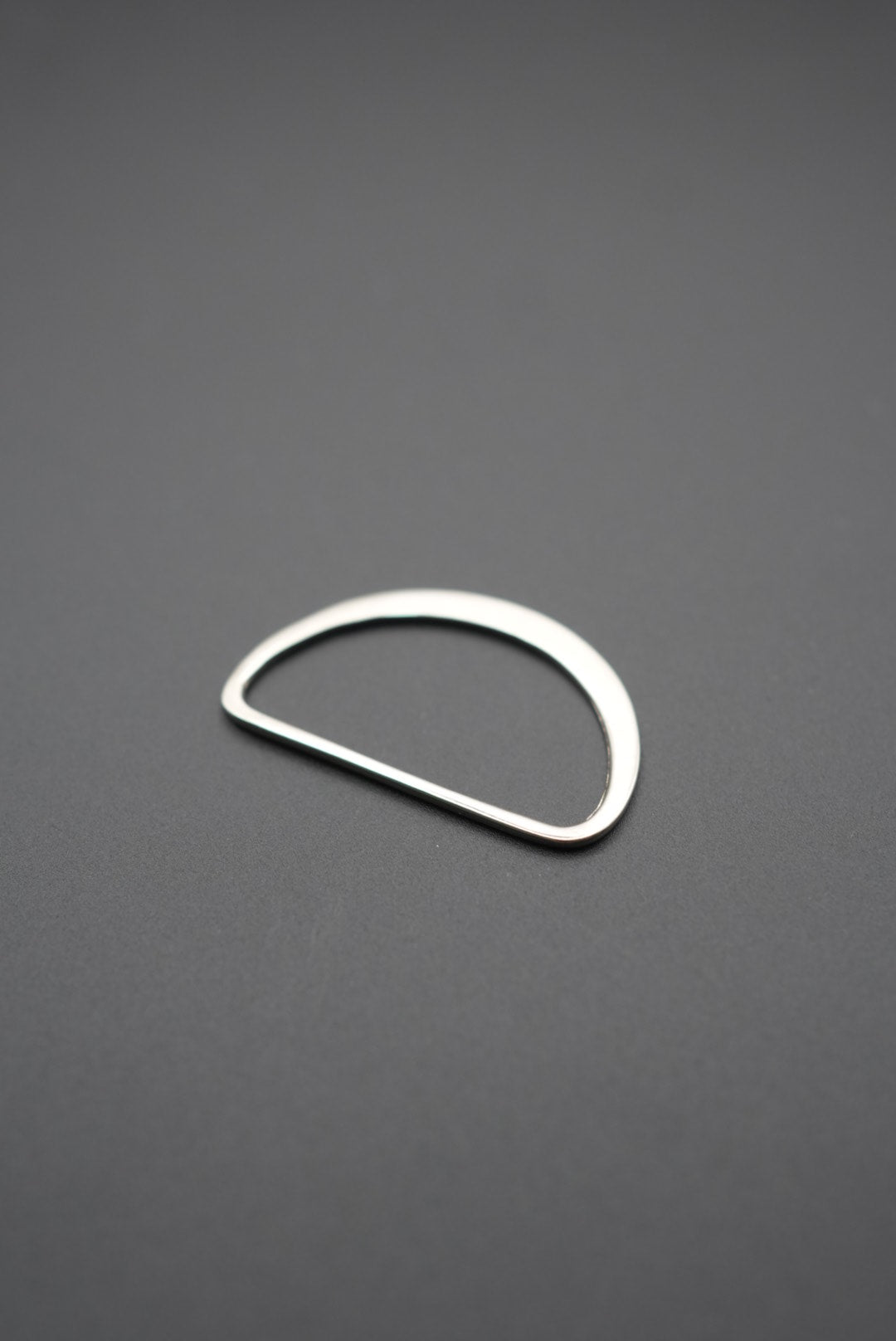 Argolla D plana metálica con acabado pulido vista inclinada sobre fondo gris
