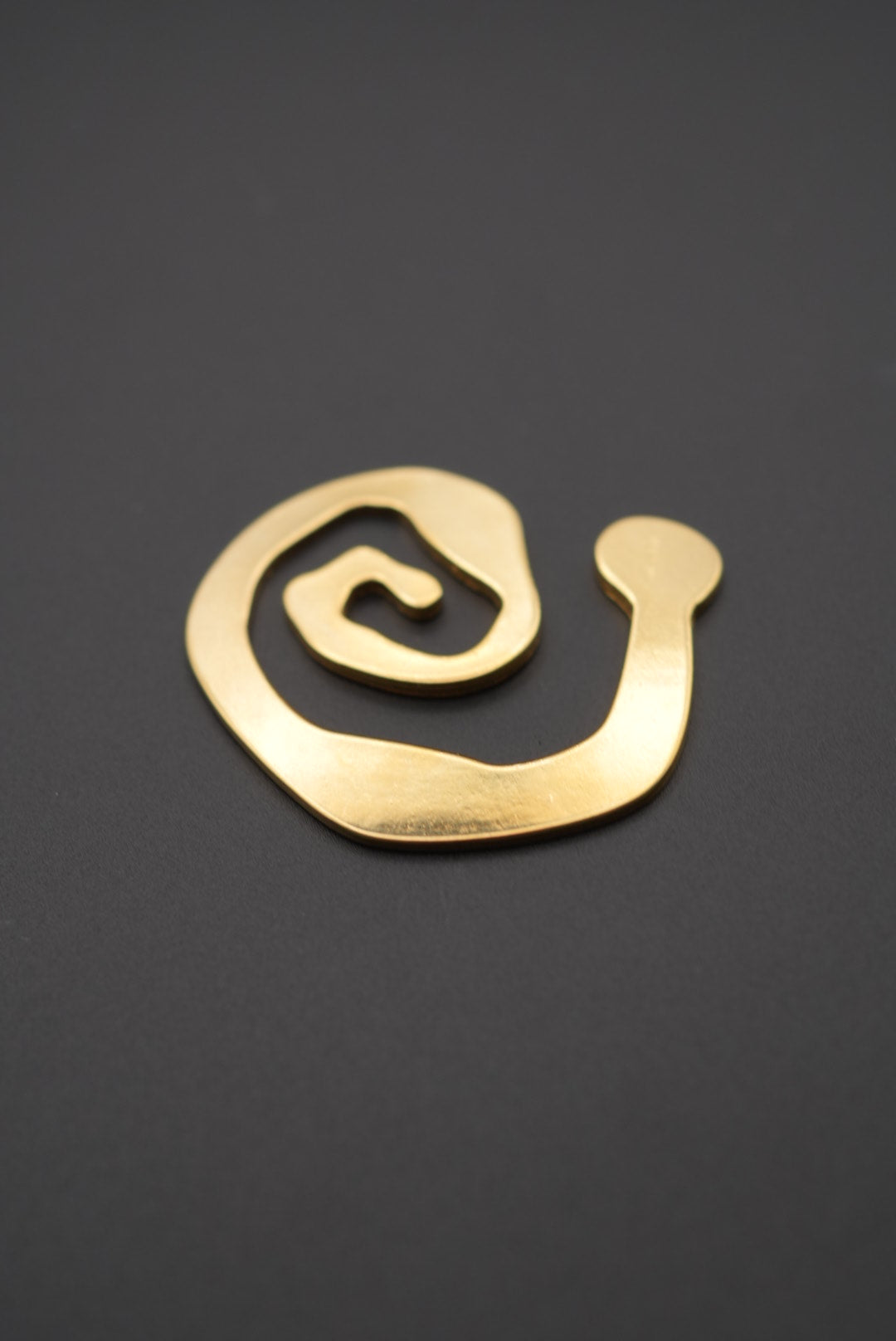 Broche espiral dorado con acabado brillante y superficie lisa sobre fondo gris