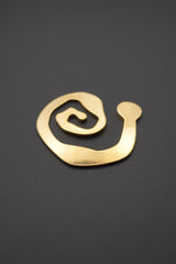Broche espiral dorado con acabado brillante y superficie lisa sobre fondo gris