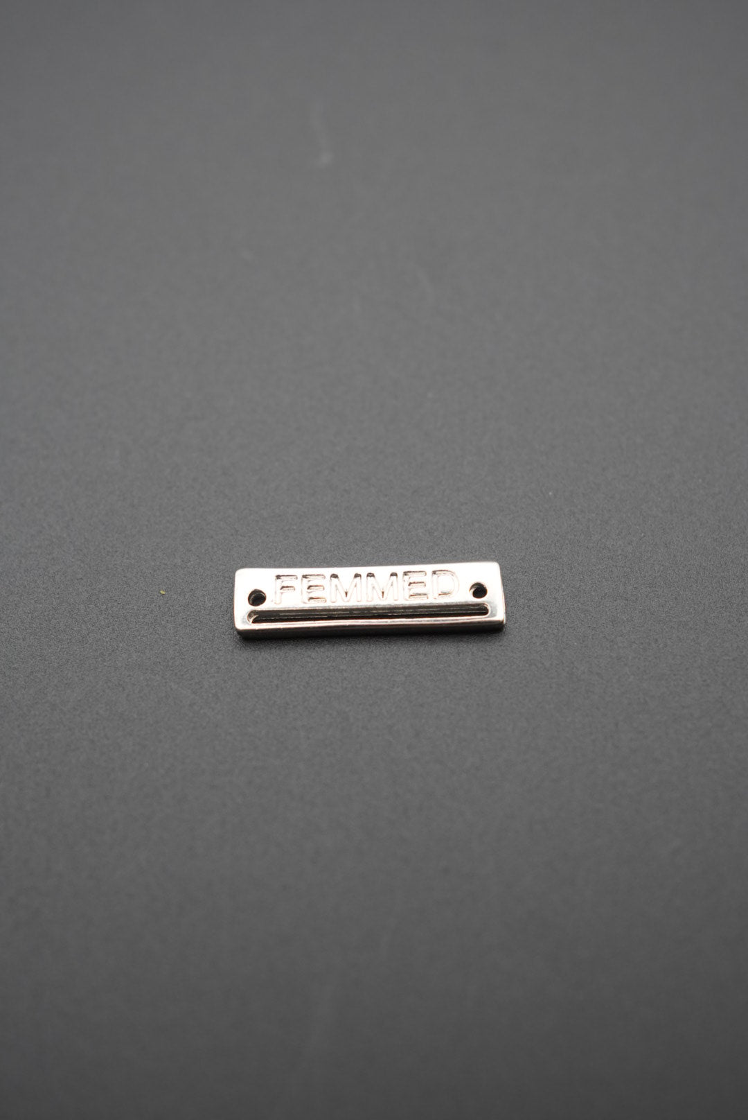 Detalle de placa de hilo metálica con logo FEMMED sobre fondo gris