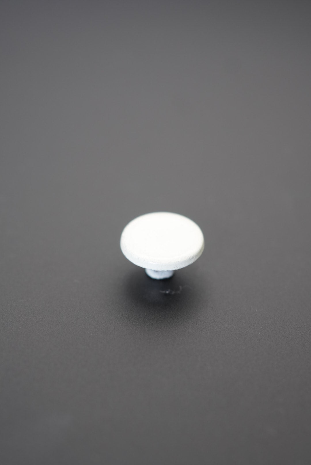 Botón metálico blanco redondo con superficie lisa sobre fondo gris oscuro
