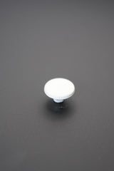 Botón metálico blanco redondo con superficie lisa sobre fondo gris oscuro