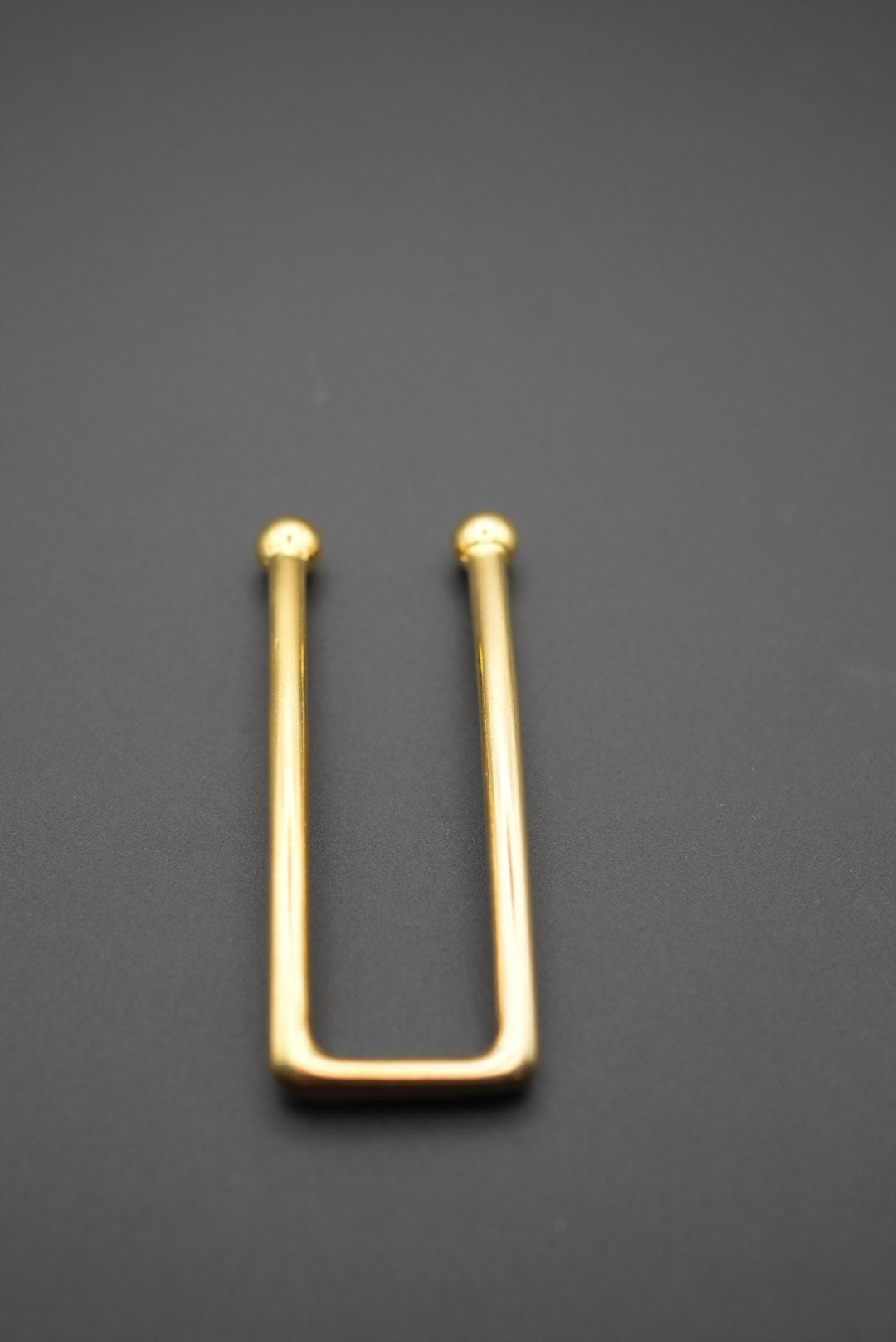 Detalle del pasador dorado rectangular sobre fondo gris oscuro