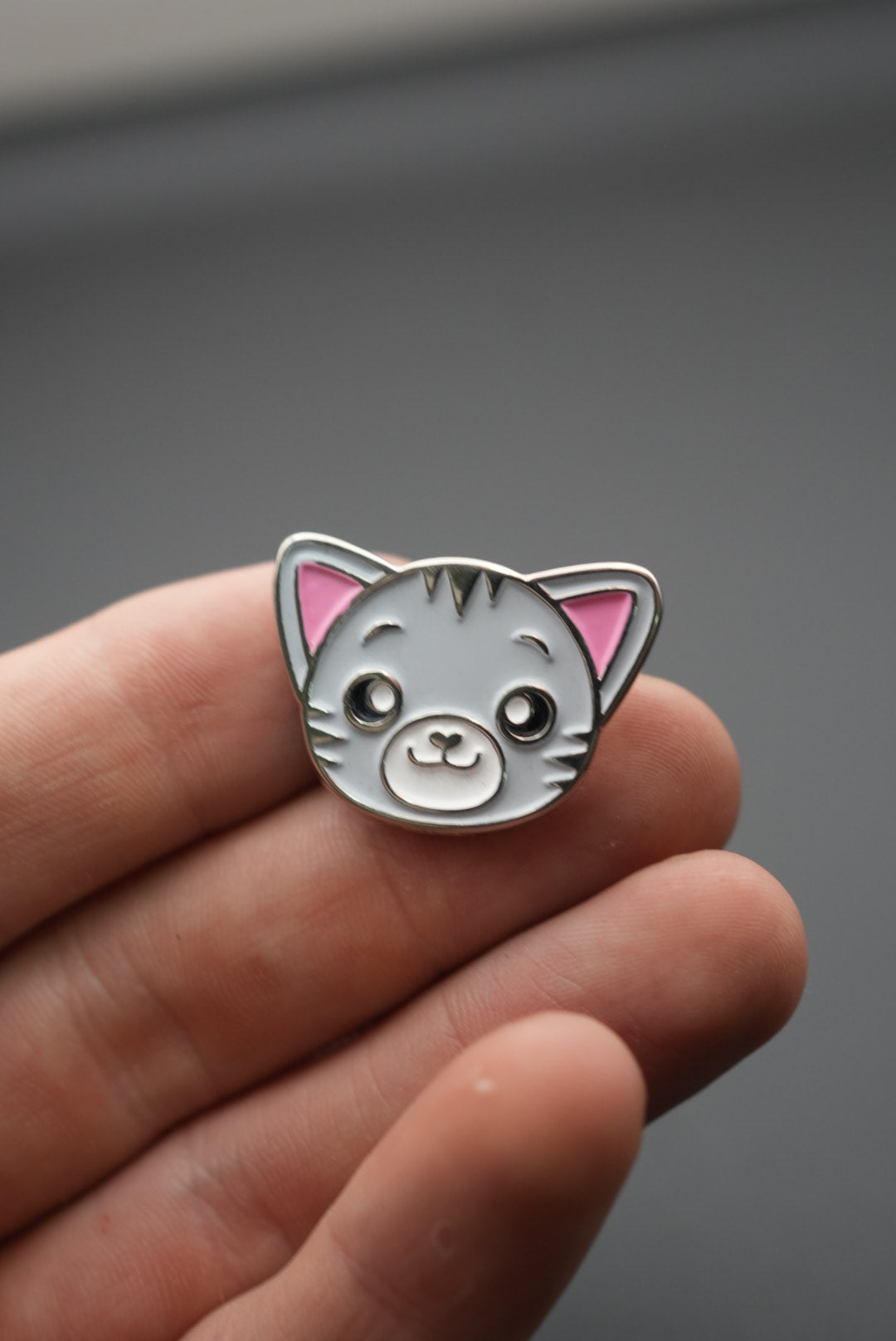 Pin de gato visto frontalmente sobre la mano con fondo gris