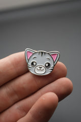 Pin de gato visto frontalmente sobre la mano con fondo gris