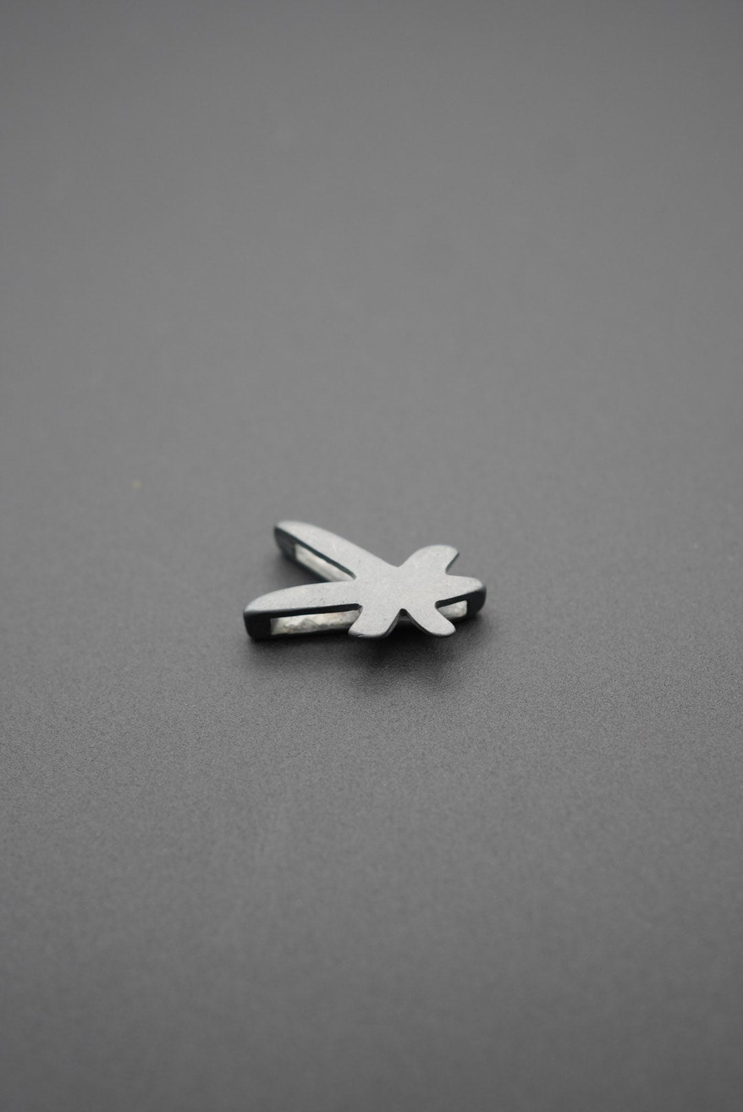 Vista frontal del pin metálico con diseño de libélula sobre fondo gris