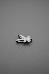 Vista frontal del pin metálico con diseño de libélula sobre fondo gris