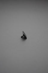 Botón de golpe negro cuadrado con vástago visto de perfil sobre superficie gris