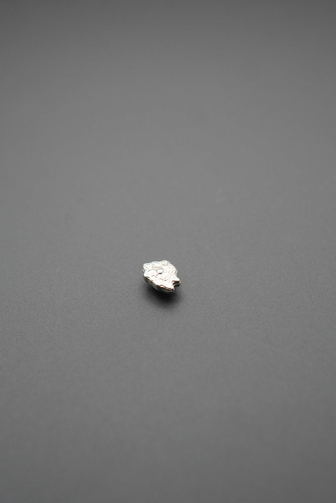 Vista lateral de pasador metálico floral plata sobre superficie gris